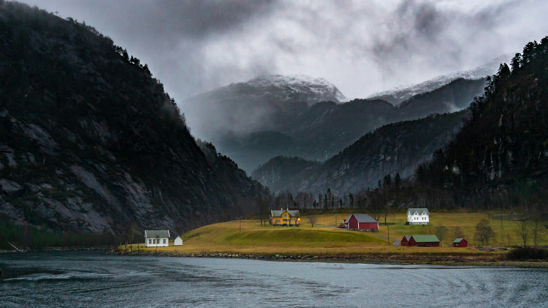 A mountain farm by the fjord under low clouds